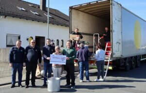 Spendenübergabe während im Hintergrund ein Hilfstransport beladen wird