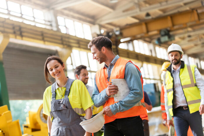 Gruppe von Arbeiterin und Arbeitern laufen in einer Fabrikhalle