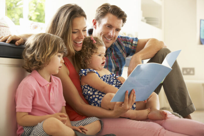 Eltern sitzen mit ihren Kindern auf dem Boden und lesen ein Buch.