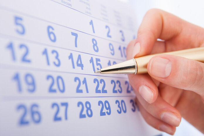Nahaufnahme einer weiblichen Hand, die auf einem Kalender ein Datum markiert