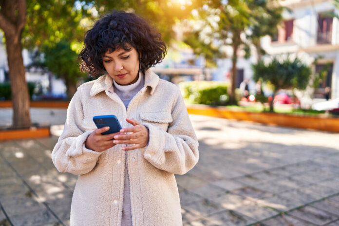 Junge hispanische Frau benutzt Smartphone mit ernstem Gesichtsausdruck im Park