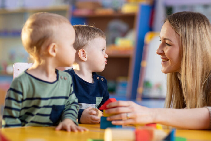 Kindergärtnerin spielt mit zwei Kleinkindern Bauklötze