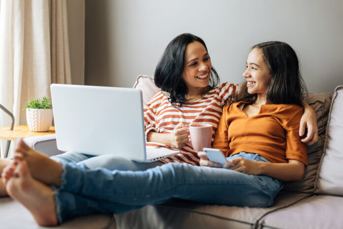 Mutter mit einem Laptop sitzt neben ihrer Teenager-Tochter auf dem Sofa